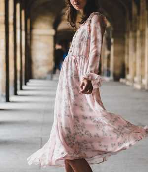 Model in long light-pink silk dress, with flower pattern, plenty of details, and an stylish finish.